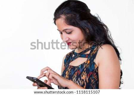 A young Indian women wearing a sleeveless dress using her smartphone , scrolling the screen with her fingers, reading a message and feeling happy