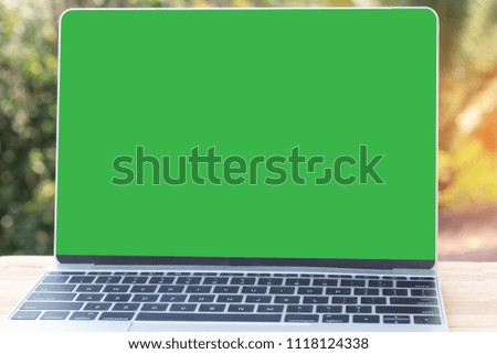 Mock up image of laptop with blank green screen on wooden table outdoor with nature background.