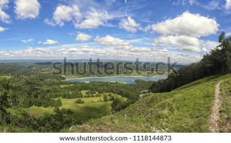 Scenic french landscape with lake, blue sky and clouds, walking path and green environment, small houses, panoramic