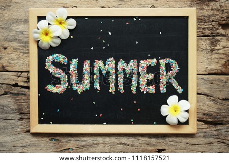 SUMMER word made from colorful gravel on black chalk board decorate with tropical flower on wooden background