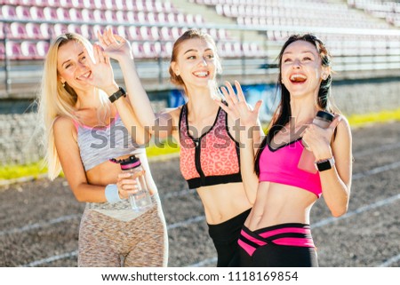 Emotional photo of group three laughing female friends with different appearance congratulate and happy to finish their morning workout at stadium track in the summer sunny evening.
