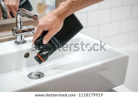 Removal of blockage in the sink, the hand of a man with a bottle of a special remedy with granules. Clean the blockages in the bathroom with chemicals. Royalty-Free Stock Photo #1118179919
