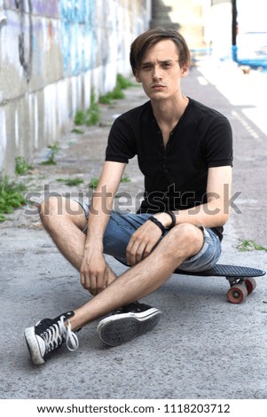Outdoor portrait of modern handsome  young man sitting on a skateboard in the street