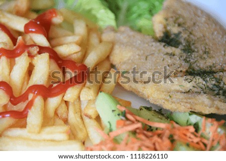 fries topped with ketchup and a salad of fresh cucumber and grated carrot fried fish