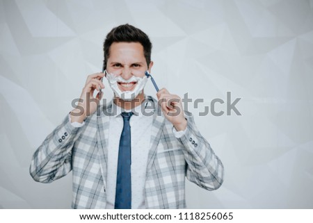 A smiling man of pleasant appearance shaves his face with a machine tool. Advertising of shaving accessories
