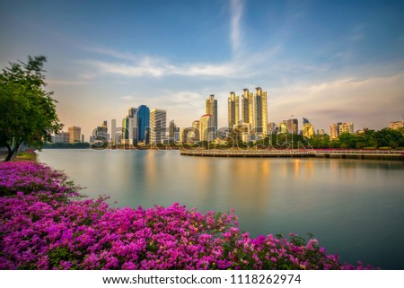 Lake Ratchada situated in the Benjakitti Park with beautiful flowers in the foreground and modern high rise buildings in the background in midtown Bangkok, Thailand. Long exposure.