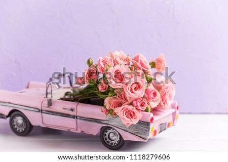 Retro car toy with pink roses flowers against  violet textured  wall. Romantic background. Selective focus. 