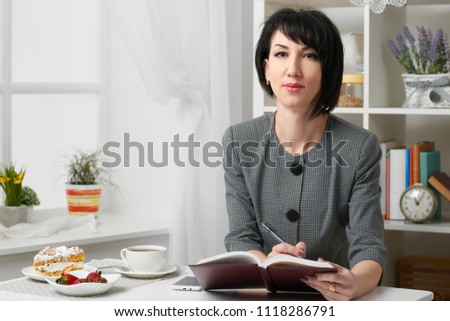 the business woman reading the diary, dressed in a gray suit poses in front of a white wall