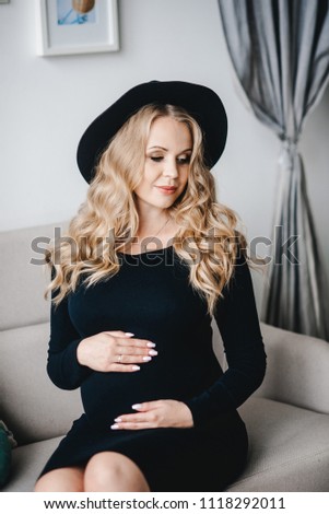 Happy pregnant young woman waiting for a child. woman dressed in black dress and hat 