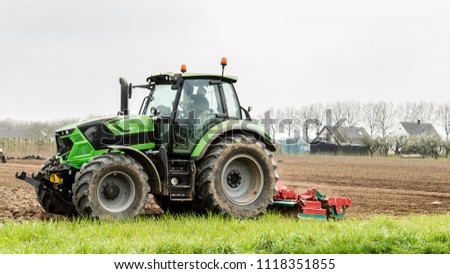 Farmer riding a green  tractor plowing his famrland with a plowing machine Royalty-Free Stock Photo #1118351855