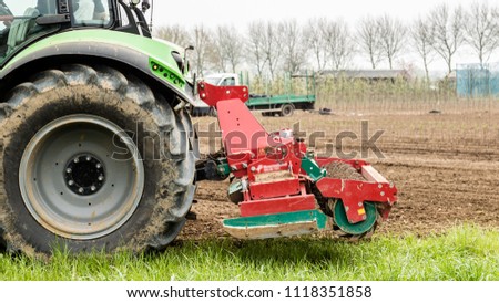 Farmer riding a green  tractor plowing his famrland with a plowing machine Royalty-Free Stock Photo #1118351858