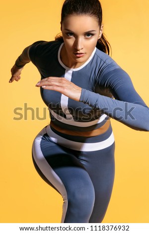 Attractive woman runner in fashionable sportswear on yellow background. Dynamic movement. Close up. Sport and healthy lifestyle
