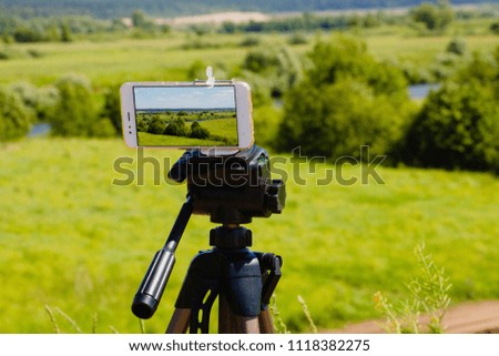 Smartphone on tripod capturing summer landscape with blue sky and meadow
