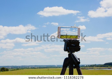 Smartphone on tripod capturing summer landscape with blue sky and meadow