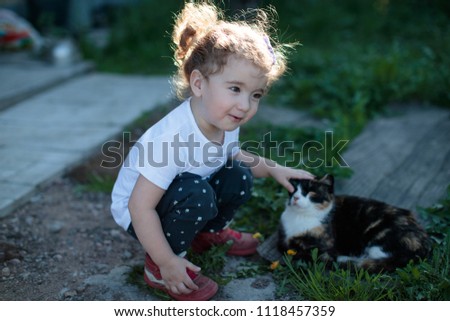 little baby girl squatting next to a cat in the yard