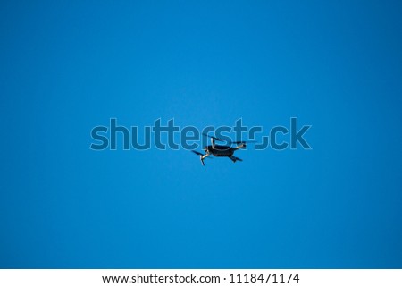 Drone flying to take aerial photo. Silhouette on a clear blue sky.