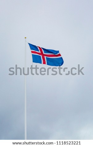 A civil flag and ensign Iceland against a clouded sky. The civil national flag of Icelanders is blue as the sky with a snow-white cross, and a fiery-red cross inside the white cross.
