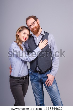 Beautiful young woman and young man are standing in an embrace on a gray background in the studio