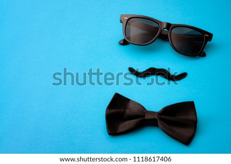Father day and male hipster fashion concept with minimalist image of a pair of square sunglasses, black bowtie and a fake moustache on colorful blue background with copy space