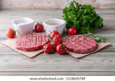 Raw hamburger cutlet on a wooden board with spices, herbs and cherry tomatoes