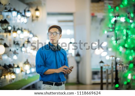 asian handsome man in casual dress with eye glasses standing and hold smart mobile phone with bokeh in foreground and background.