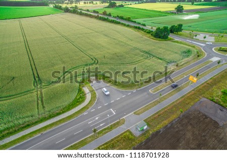 Aerial view of a road with signs and guidelines for traffic between a new development area for an industrial estate and an arable area with green wheat, Germany