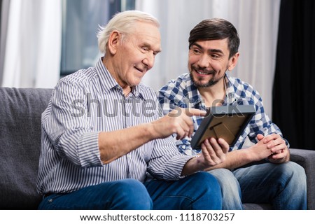 Good memory. Cheerful aged father and his son sitting on the sofa while holding a photo frame Royalty-Free Stock Photo #1118703257