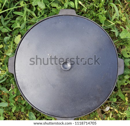 Large metal  black  pot with a lid for roasting of meat and vegetables is located on grass. Top view outdoor shot. 