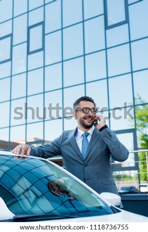 portrait of smiling businessman talking on smartphone while standing at car on street