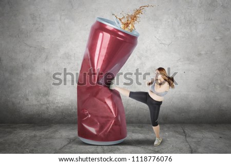 Picture of fat woman wearing sportswear while kicking a can and refusing soft drink