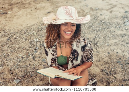 Woman portrait sitting on the beach and reading book while smiling widely