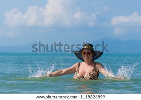 Woman in black hat posing in the sea and splashing water
