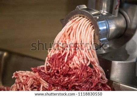 Horizontal close-up color image of process of grinding/preparation of minced raw red meat in Grinder.