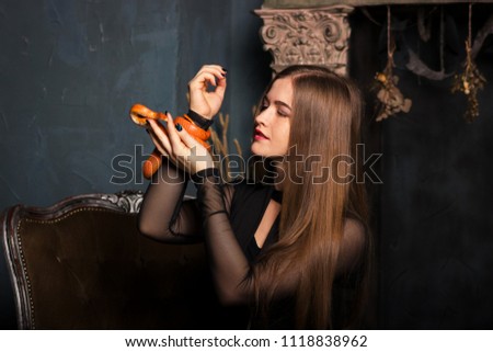 Beautiful young woman in black dress sits on a chair with orange corn snake and looks at it