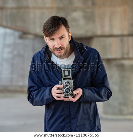 bearded photographer photographs with enthusiasm the film camera.  Photographing a two-objective old camera on location.