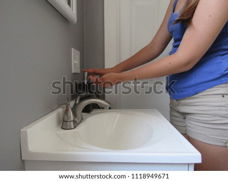 Woman pushing down on a soap dispenser to wash her hands in the sink 