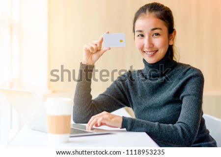 Asian attractive happy smart smile business woman holding credit card and use laptop for shopping online on e-commerce website in the morning time with a cup of coffee.