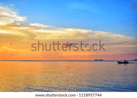 Colorful sunset into the ocean with the silhouette of fisherman boat. Image has grain or subject blurry or noise and soft focus when view at full resolution.