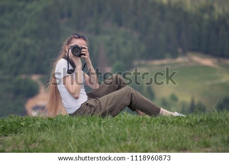 Girl with the camera sits on a hill and photographs. Forest on background