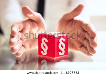 Close-up Of A Person's Hand Protecting Red Cubic Block With Paragraph Symbol