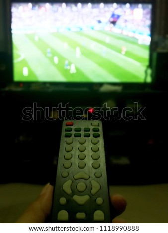 watching a football match on TV and close-up photo of the hand holding the remote control. Blur picture of football game on TV.
