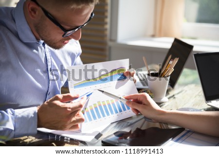 Young Businessman Analyzing Graph With His Partner At Workplace