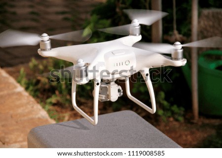 White quad copter Drone with 4K digital camera is take off and to fly high in air, to take photos and record footage from above. Drone with four motors, propellers, camera and red warning lights.