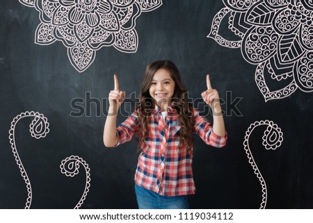 Looking good. Excited girl smiling and feeling happy while pointing to the marvelous paintings on the wall of her bedroom