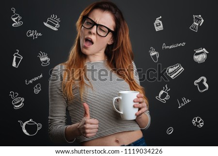 Feeling good. Expressive young beautiful woman winking her eye and feeling good while drinking tasty coffee