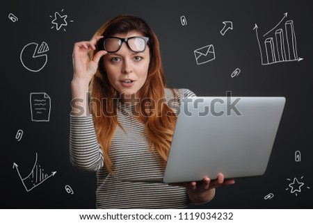 Clever woman. Clever experienced economist standing with a laptop in her hands and touching the glasses