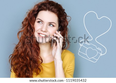 Friendly phone talk. Positive pretty student smiling and looking glad while talking on the phone with her friend