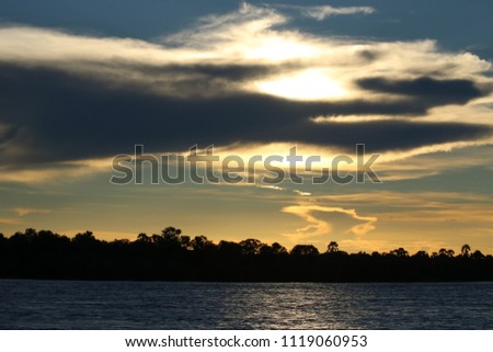 Sunset in the Zambezi River, Zambia and Zimbawe border, with some clouds around taken from the water, Africa Royalty-Free Stock Photo #1119060953