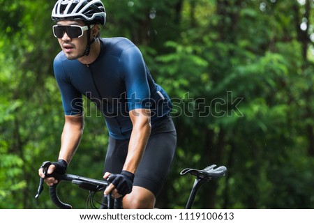 Close up on Asian man in blue cycling jersey isolated on blurred forest background. Concept for morning ride. Royalty-Free Stock Photo #1119100613