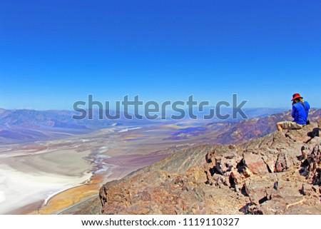 Man photographer sitting on the rock, taking picture of beautiful view on Badwater Basin from Dante's view point. Death Valley National Park, California, USA.